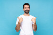 © luismolinero - Young man with beard  over isolated blue background with thumbs up gesture and smiling
