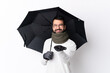 © luismolinero - Caucasian handsome man with beard holding an umbrella over isolated white wall holding copyspace imaginary on the palm to insert an ad