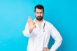 © luismolinero - Young caucasian man over isolated background wearing a doctor gown and making stop sign