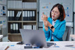 © Tj - Businesswoman experiencing wrist pain while working long hours on a laptop in an office, indicating symptoms of carpal tunnel syndrome or a work-related injury