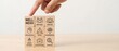 © Karla - Hand selects a wooden block labeled 'wellness' from a grid showcasing various essential dimensions of holistic well-being.