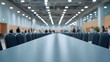 © Wuttichai - A long empty conference table and chairs in a modern meeting hall with blurry figures in the background