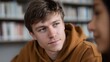 © Wuttichai - Young man with blue eyes in a library wearing a brown hoodie looking thoughtfully towards someone off