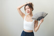 © KMPZZZ - Suffering summer heat wave stroke, hot weather, tired asian young woman sweaty and thirsty, refreshing with hand in blowing, wave fan to ventilation when temperature high, isolated on background.