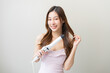 © KMPZZZ - Beautiful curly brunette, attractive asian young woman, girl smiling using curler, curling iron long hair with ceramic curler straightener at home. Hairstyle and Hairdressing. Beauty and hair care.