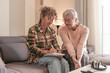 © luciano - Smiling Senior woman and Caregiver Sharing a Moment sitting together on sofa at home. Concept of assistance and help to our elderly