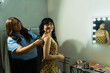 © AntonioDiaz - Professional stylist supporting young woman backstage, adjusting her dress before a fashion event with makeup table nearby