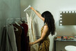 © AntonioDiaz - Model selecting clothing from a garment rack, preparing for a fashion show backstage with a vanity mirror