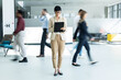 © Dejan - Businesswoman standing still and focusing on digital tablet, ignoring motion blurred colleagues walking fast around her in a modern office