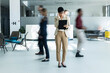© Dejan - Professional businesswoman concentrating on her digital tablet in a busy, modern office lobby with people in motion blur