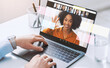 © Prostock-studio - A man types on a laptop with a blank screen while engaging in a video call. Sunlight shines through the window. Several faces are visible on the screen in a virtual meeting setup.