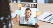 © Prostock-studio - A woman sits at a table in her home office. She looks at a tablet with a virtual meeting. Colleagues are visible on the screen. This scene shows modern remote work life and technology use.
