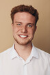 © SHOTPRIME STUDIO - Smiling young man with red hair and freckles wearing white shirt looks at camera on beige background. Portrait of confident male model with natural skin and friendly expression.