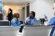 © DC Studio - African American woman smiles while receiving good news from healthcare worker reviewing checkup results on laptop. Black female patient sits in hospital lobby, discussing follow up plans with nurse.