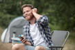 © auremar - smiling young man tourist using smartphone next to tent