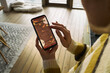 © DragonImages - Caucasian middle aged woman using smartphone, holding device in left hand while scrolling with right index finger, reading mulled wine recipe displayed on screen indoors