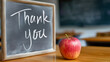 © Tetyana - Chalkboard with thank you message and a fresh red apple on a wooden desk, symbolizing appreciation for education and teachers in a school classroom setting, copy space
