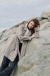 © SHOTPRIME STUDIO - Young woman in knitted coat leans on rocks outdoors, eyes closed, enjoying peaceful moment. Calm nature setting with muted colors and soft natural light.