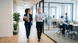 © solom - diverse business colleagues walking and talking in modern glass office corridor with professional team working in background meeting room during corporate workday morning
