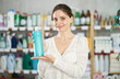 © JackF - Smiling young woman deciding which shampoo or shower-gel to buy in retail store