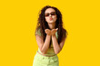 © Pixel-Shot - Young African-American woman in sunglasses blowing kiss on yellow background