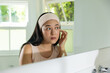 © Wavebreak Media - Adult Asian woman wearing headband examining eye, touching temple at bathroom sink with dropper