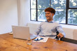 © wavebreak3 - Male in blue shirt sitting at meeting table checking chart while typing on laptop near smartphone