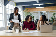 © Wavebreak Media - Diverse female colleagues studying charts with tablet and typing on laptop at table in open office