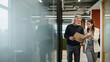 © kabzarchyk - Junior associate eagerly pointing out a critical overlooked detail in a physical case file to a concentrated senior partner during a brief hallway consultation.