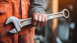 © Khadam Hussain - A close-up of a worker's hand holding a large adjustable wrench in a workshop setting.