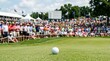 © Nazlykhan - Golf ball on green with crowd in background at tournament. Golfing hobby and professional sport competition. Spectator watching game on golf course. Active lifestyle and leisure activity.