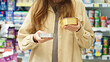 © Pavel - Woman choosing pet food in store, comparing options before purchase, selecting canned wet food for dog or cat, consumer decision making in pet shop