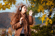 © _KUBE_ - Mid shot of a happy young woman in a coat listening to music with headphones, singing and dancing in park. Concept of happiness and freedom