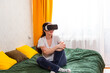 © _KUBE_ - Female embracing the evolution of virtual reality gaming while relaxing indoors, testing high-end simulations, sitting on bed