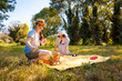 © _KUBE_ - Young daughter and her Caucasian mother sitting in a sunny park on a picnic blanket enjoying quality time, games, and family holiday outdoors. Low angle view