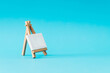 © Jakov Ilkoski - Blank canvas on wooden easel on light blue background. Minimal art mockup. Branding presentation idea. Creative copy space.