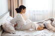 © Anastasiya - Pregnant Black woman sitting on bed holding her lower back in pain, side profile view. Back pain during pregnancy concept in calm bedroom interior