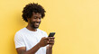 © aosa - Smiling Black man using smartphone on a bright yellow background with copy space