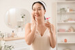 © Pixel-Shot - Beautiful young happy Asian woman with cotton pad and bottle of micellar water in bathroom