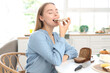 © Pixel-Shot - Beautiful young happy woman eating tasty toast with fresh butter in kitchen at home