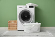 © Pixel-Shot - Modern washing machine with baskets and laundry near green wall