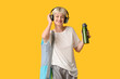 © Pixel-Shot - Sporty young woman with yoga mat, headphones and bottle of water on yellow background