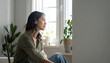 © Teeradej - Mental wellness, depression. Thoughtful woman sits by window, gazing outside with serene expression