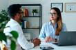 © Seventyfour - Young adult businesswoman consulting male client across desk, discussing strategy in office with laptop. Ideal for business advisory, professional services, client meeting marketing