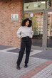 © Caser - woman posing outside modern storefront near brick wall in casual autumn outfit