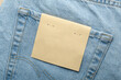 © SOLDATOOFF - Blank kraft paper label lies on back pocket of light blue jeans and fits fashion branding, clothing tag mockup, and retail use.