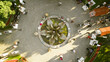 © AmazingAerialAgency - Aerial view of people gathering around a circular fountain with metallic leaves and yellow flowers, surrounded by tables and chairs, creating a vibrant social space. Sremska Mitrovica, Serbia.