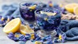 © Alfath - Two glasses of vividly colored herbal infusion garnished with citrus slices rest on a textured surface surrounded by fallen flower petals.