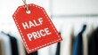 © K1drock - Red sale tag with HALF PRICE text hanging in clothing store, sharp retail discount label close-up with paper texture and soft boutique bokeh