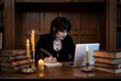 © Schizarty - Gothic student with vampire beauty studying at dark wooden desk using laptop and writing with quill pen by candlelight in library